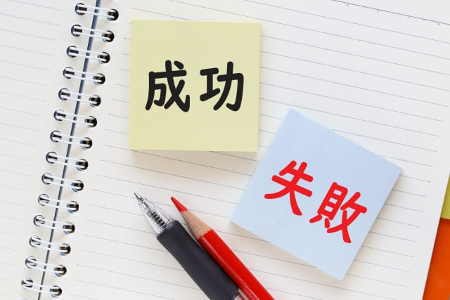 見開きの真っ白なノートの上に「成功」と印字された黄色の付箋と「失敗」と印字された青色の付箋と赤鉛筆とボールペン