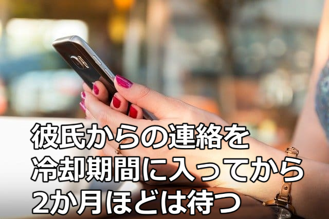 「彼氏からの連絡を冷却期間に入って位から2か月ほどは待つ」の文字と赤のマニュキュアを塗った女性がスマホを持っている