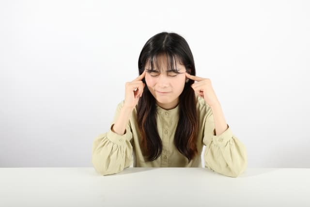 こめかみに人差し指をおいて悩む女性